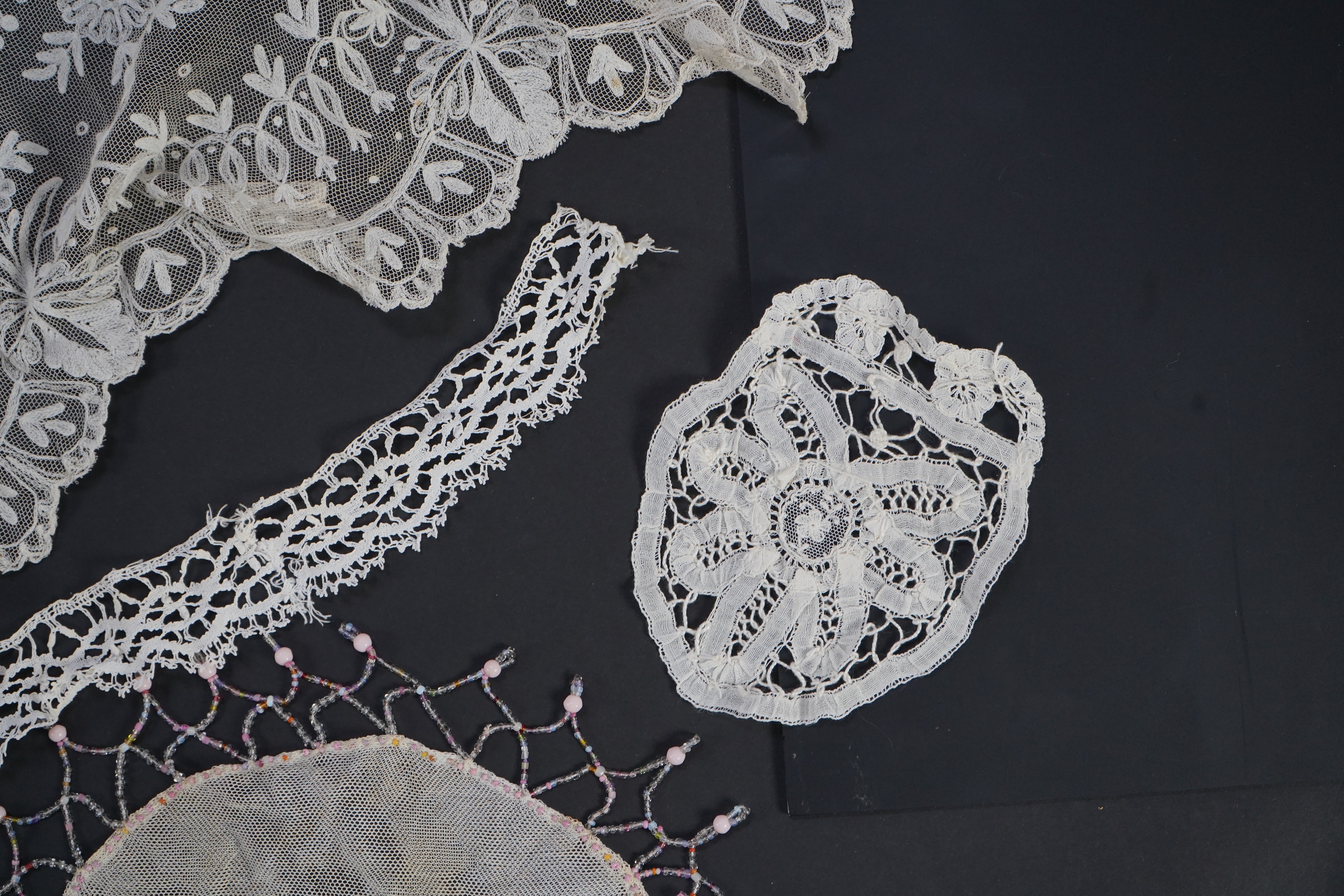 A white tape lace on net bed cover, a cream lace needle run panel, three Brussels bobbin lace collars, a lappet and two beaded tea pot covers, bed cover 200cm x 250cm. Condition - the bedcover has damage to the netting,